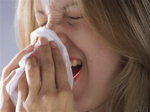 Woman sneezing into a tissue.